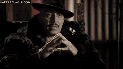 a man wearing a hat and a fur coat is sitting in a chair .