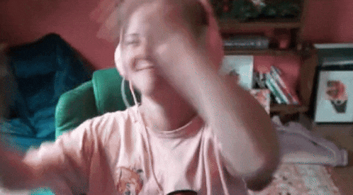 a woman wearing headphones and a pink shirt is smiling and dancing