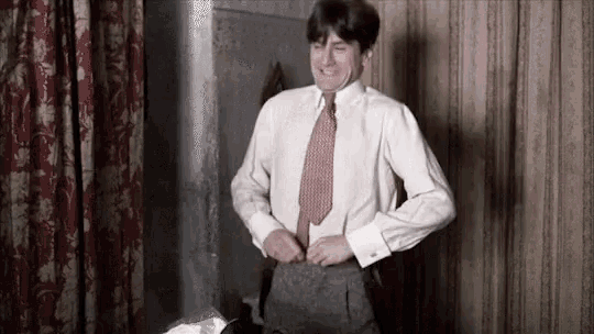 a man in a white shirt and red tie is standing in a room adjusting his pants .