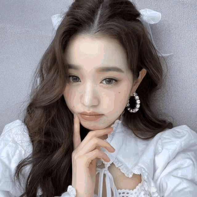 a woman wearing a white dress and hoop earrings has her hand on her chin