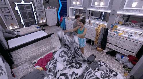 a woman in a green tank top is holding a blanket in a messy bedroom