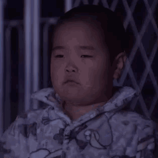 a little boy is sitting in a dark room with chinese writing on it