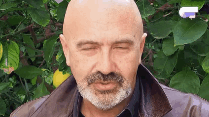 a bald man with a beard is making a funny face while wearing a leather jacket .