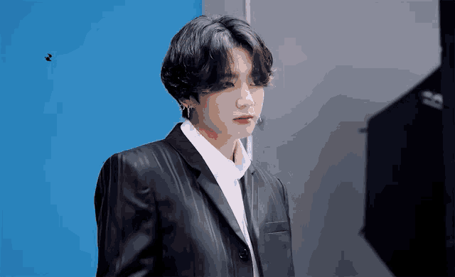 a man in a black suit and white shirt stands in front of a blue background