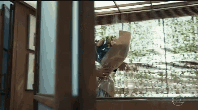 a woman is holding a large bouquet of flowers in front of a window
