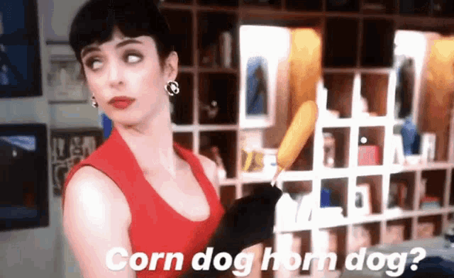 a woman in a red tank top is holding a corn dog and asking " corn dog horn dog "