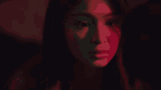 a close up of a woman 's face in a dark room with red and blue lights behind her .