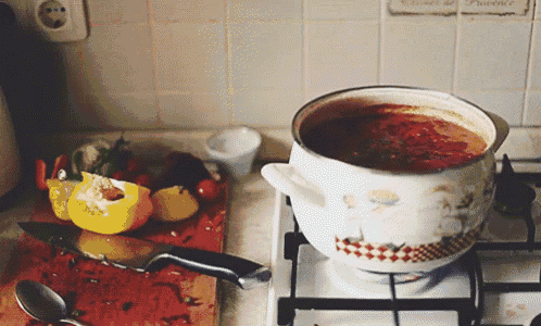 a pot of soup sits on a stove next to a cutting board with vegetables on it