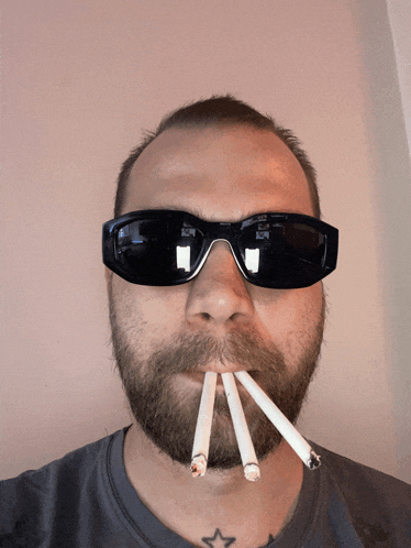a man with a beard wearing sunglasses has three cigarettes sticking out of his mouth