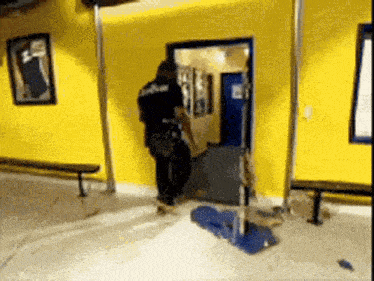 a man in a police uniform is standing in a room with a yellow wall and a blue door .