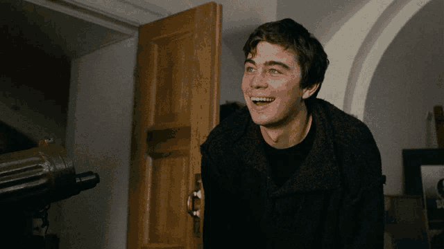 a young man in a black sweater is smiling in front of a wooden door