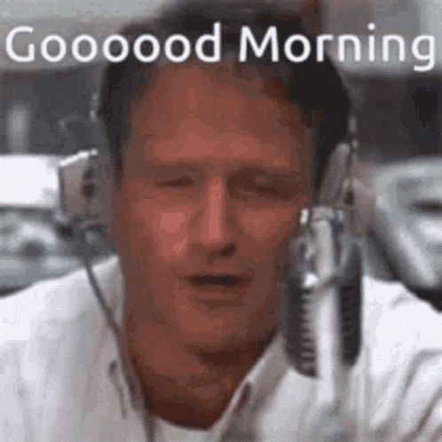 a man wearing headphones is talking into a microphone and saying `` good morning '' .