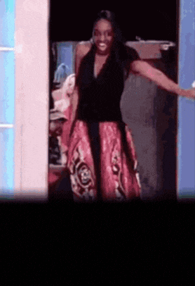 a woman in a black top and red skirt is standing in a doorway .