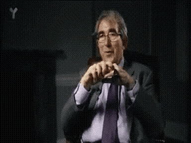 a man in a suit and tie is talking in front of a black background with the letter y on it