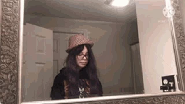 a woman with purple hair and glasses is looking at herself in a mirror .