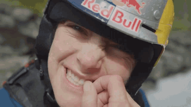 a man wearing a red bull helmet bites his finger