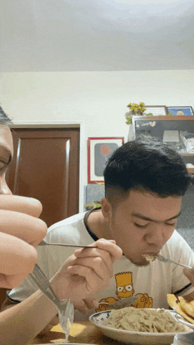 a man wearing a shirt with bart simpson on it eating spaghetti