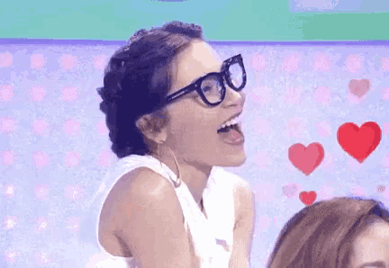 a woman wearing glasses and a white tank top is laughing with her tongue out .