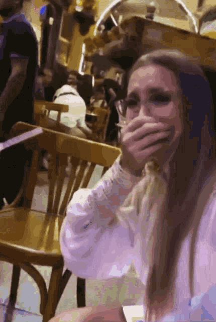 a woman covering her mouth with her hand while sitting at a table