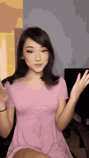 a woman in a pink dress is sitting in a chair waving