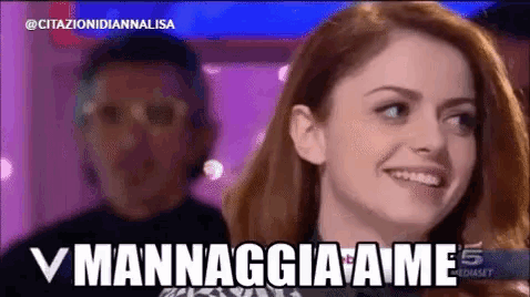 a woman is smiling in front of a man with the words v mannaggiame written on the screen behind her