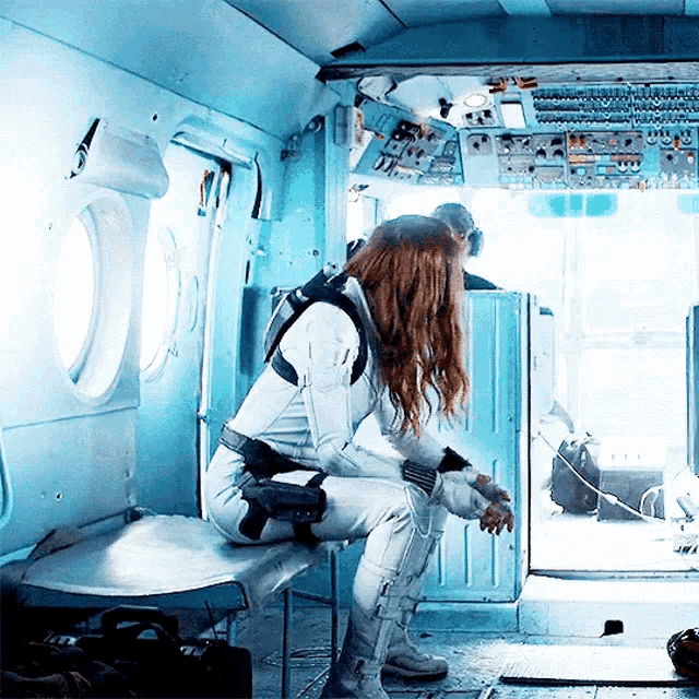 a woman in a white suit sits on a bench in a plane