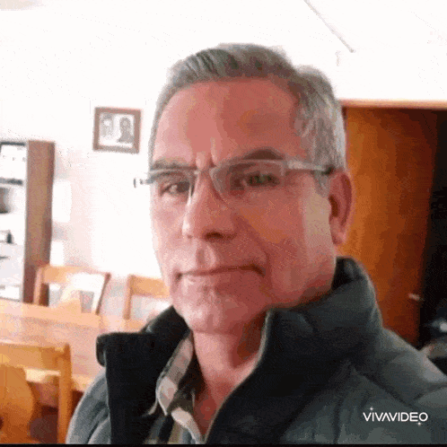 a man wearing glasses and a jacket is making a funny face .