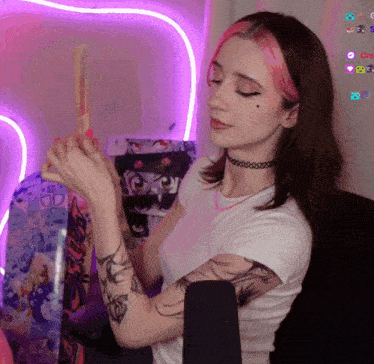 a woman with pink hair and a choker holds a stick