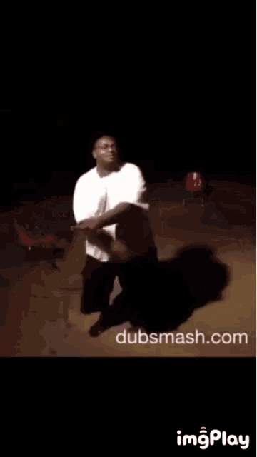 a man in a white shirt is dancing in a dark room with a chair in the background .