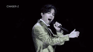 a man in a green suit is singing into a microphone on stage .