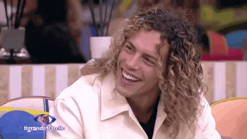 a man with curly hair is smiling in front of a sign that says grande fratello