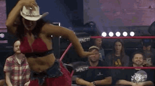 a woman in a cowboy hat is in a wrestling ring with a crowd watching .