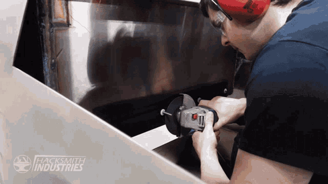 a man wearing red ear muffs is working on a piece of metal with a hacksmith industries logo in the background