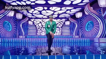 a man in a green jacket and sunglasses is dancing on a stage in front of a pool of water .