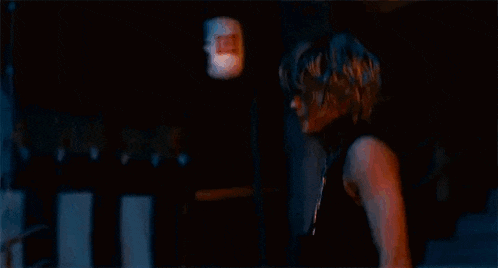 a man is standing in a dark room wearing a black tank top and a necklace of beads .