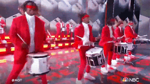 a group of men in red suits are playing drums on a stage