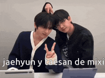 two young men are sitting next to each other at a table giving the peace sign .