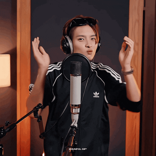 a person wearing headphones and a black adidas shirt is singing into a microphone