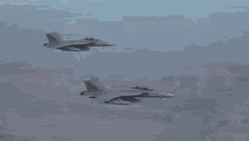 two fighter jets are flying in formation in the sky over a city .
