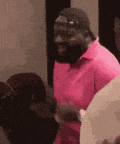 a man with a beard wearing a pink shirt and black hat