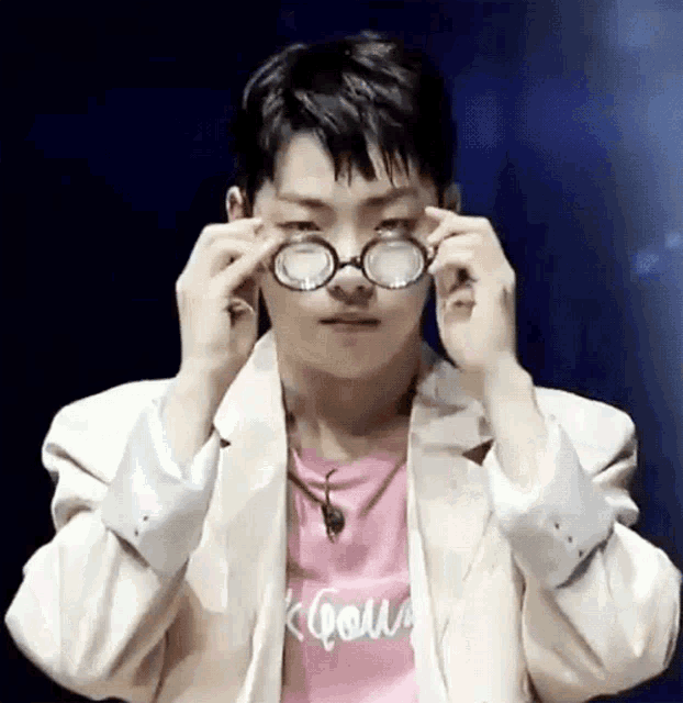 a young man wearing glasses and a pink shirt is covering his eyes with his hands .