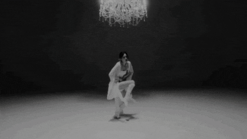 a black and white photo of a woman dancing in front of a chandelier .