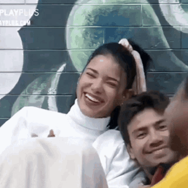 a group of people are laughing in front of a wall that says playplus.com