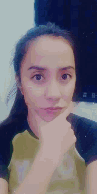 a woman with her hand on her chin is wearing a black and gold shirt