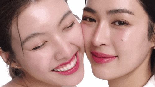 a woman with pink lipstick kisses another woman 's face