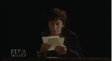a person sitting in a chair reading a piece of paper with amv written on the bottom right