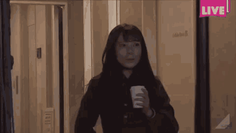 a woman is holding a cup of coffee and smiling in a room .