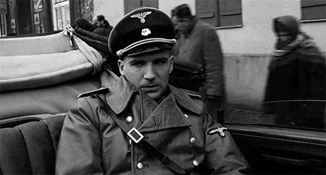 a man in a military uniform is sitting in a car and smoking a cigarette .