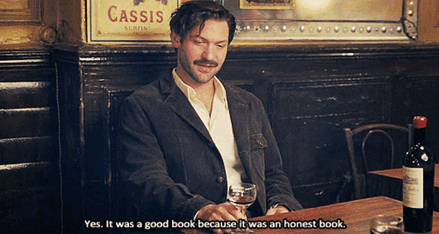 a man sits at a table with a glass of wine and a bottle of wine and says yes it was a good book because