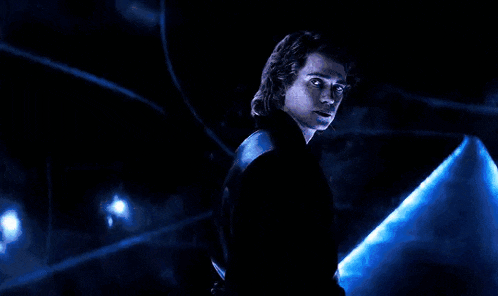 a man in a black suit is standing in the dark with a blue light behind him .